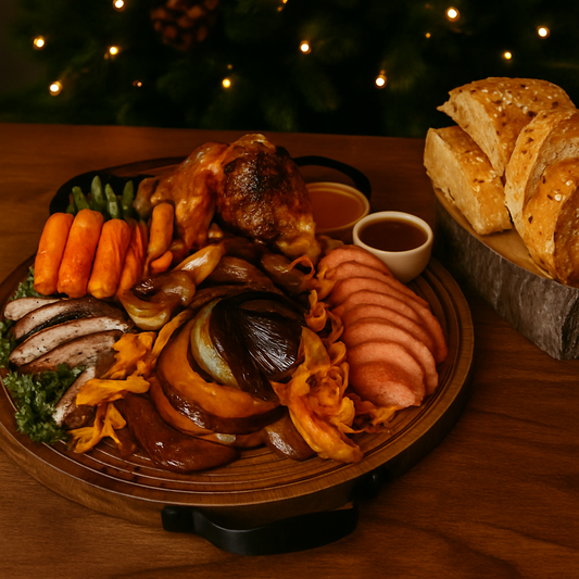 Plated meal with roasted meats, vegetables, and bread on a wooden table with a Christmas tree in the background.